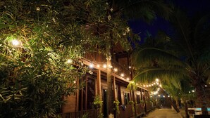 Un edificio de madera con balcón, rodeado de exuberante vegetación y palmeras, de noche.