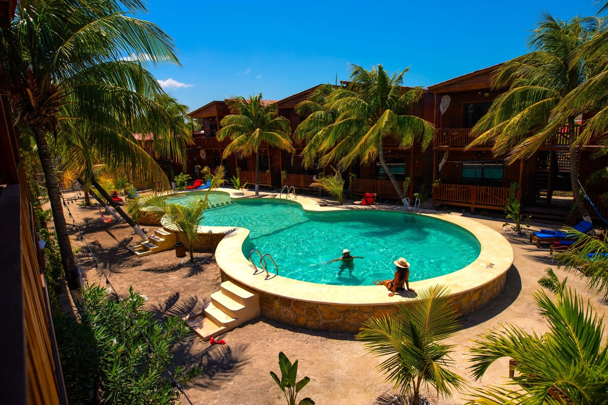 A resort with a large pool, palm trees, and wooden buildings.