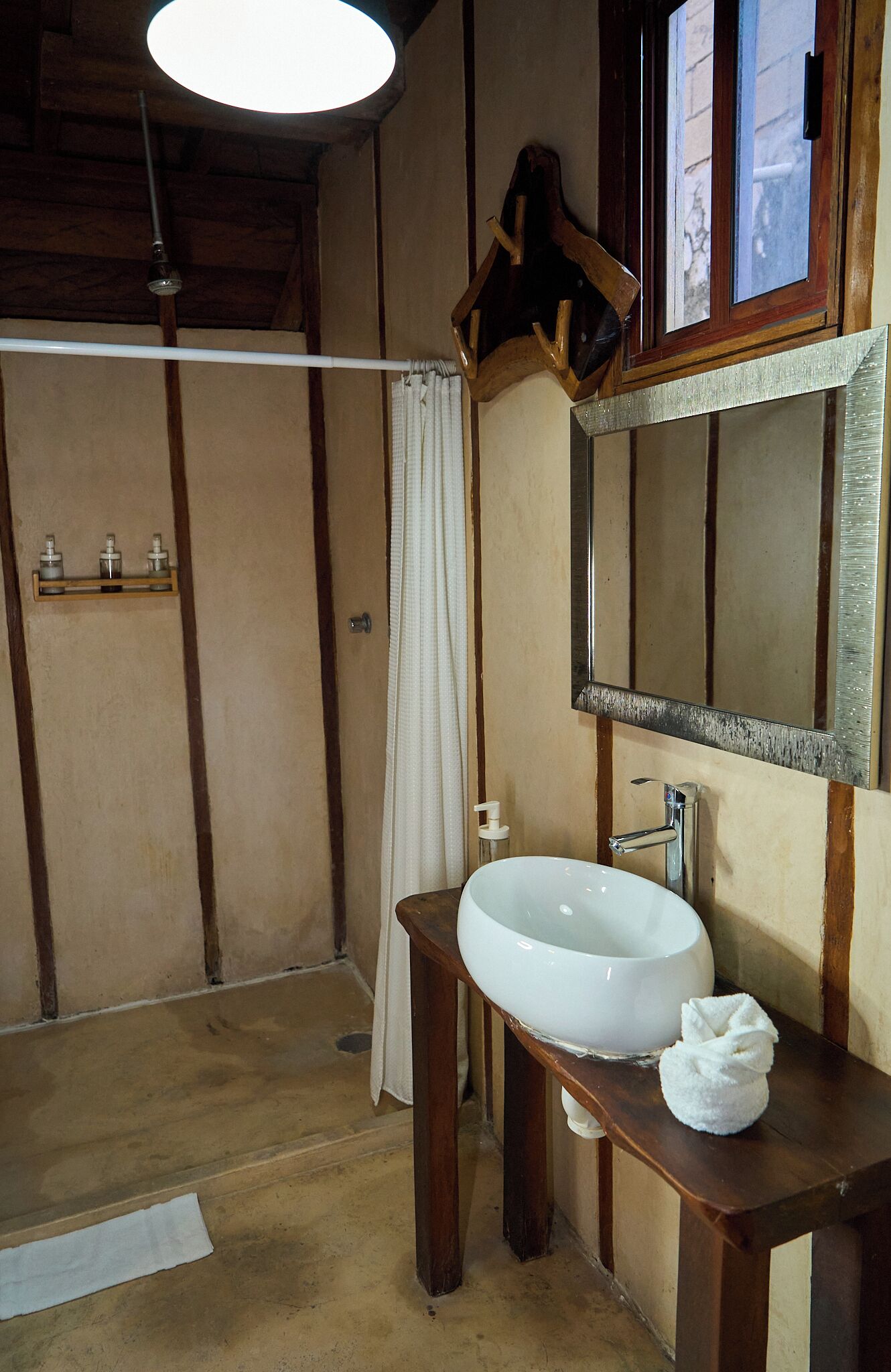A bathroom with a wooden vanity, a white sink, a mirror, and a shower area.