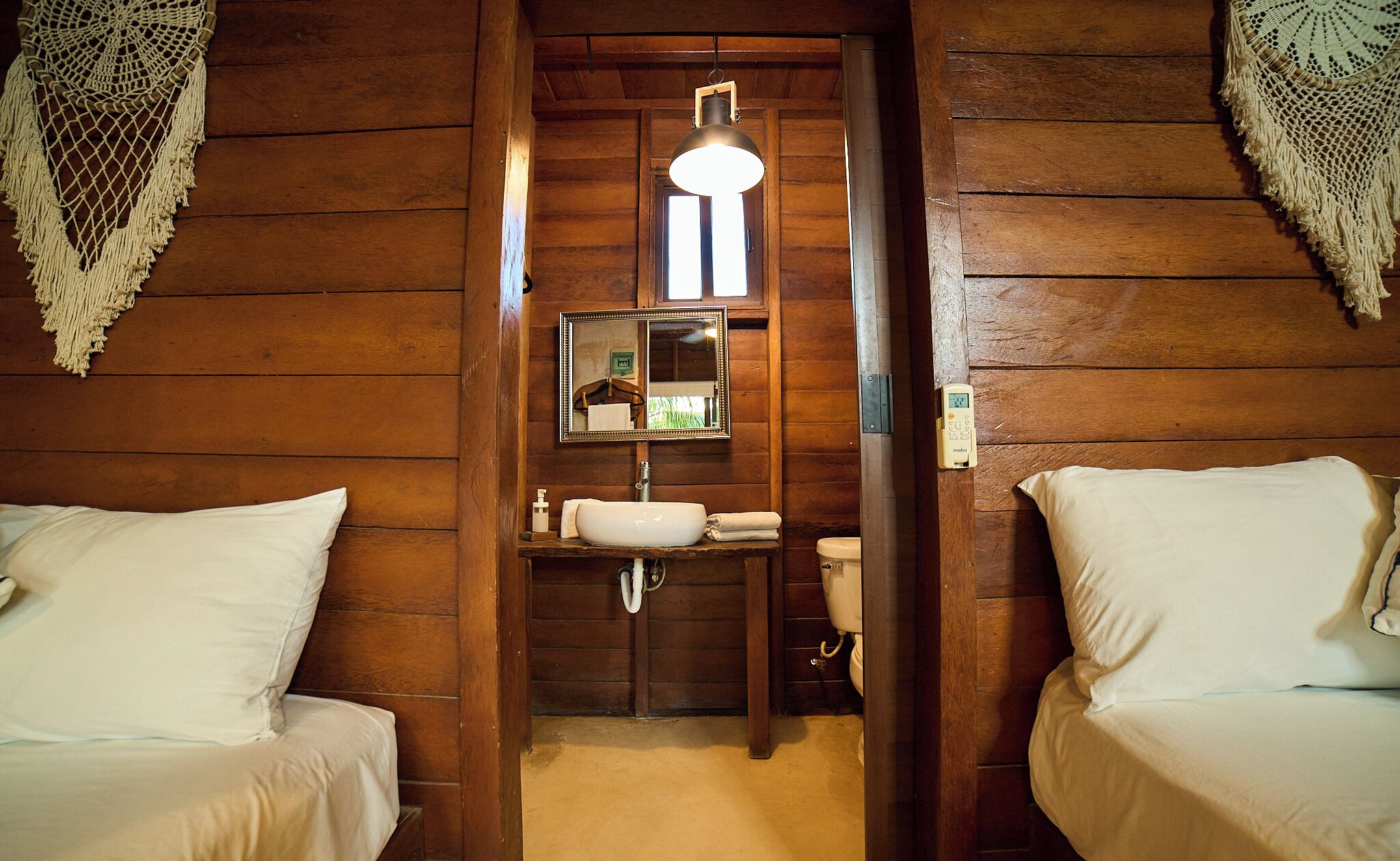 Una habitación de estilo cabaña con lavamanos central, espejo y dos camas.