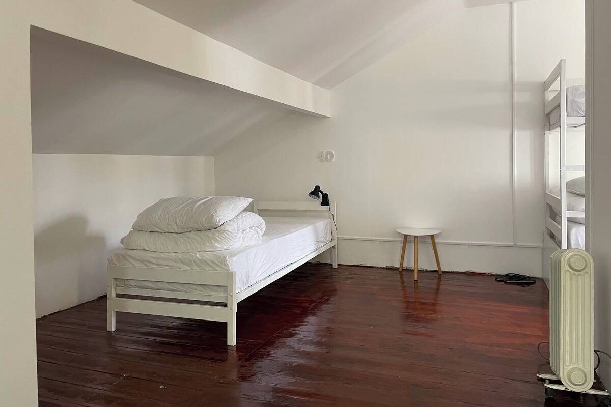 A small, white, single-bed room with a sloped ceiling, a small white table, and a radiator.