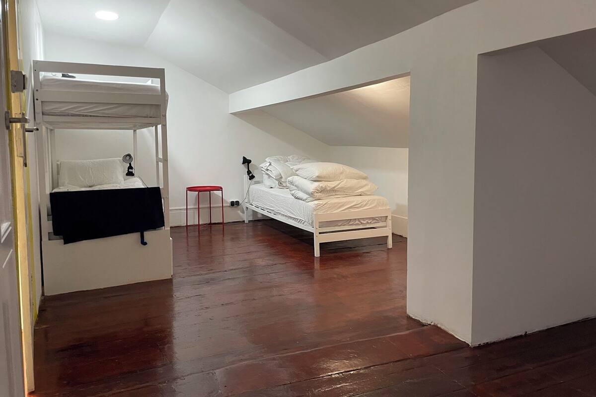 A compact room with a bunk bed, a small red stool, and a white desk.