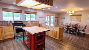 A modern kitchen with wooden cabinets, a central island, and a dining area with wooden chairs.