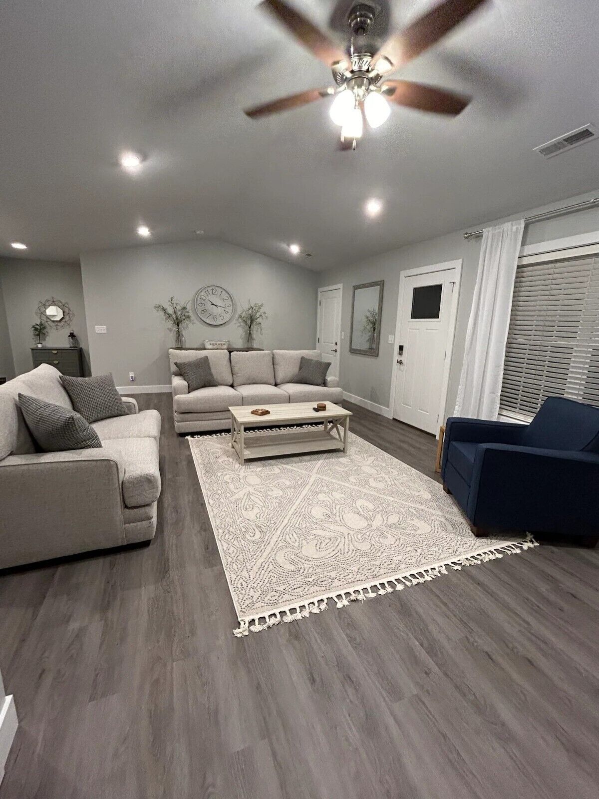 Un salon moderne avec un ventilateur de plafond, un grand tapis et un fauteuil bleu.