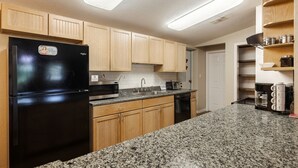 A compact kitchen with wooden cabinets, a black refrigerator, a microwave, a toaster, and granite countertops.