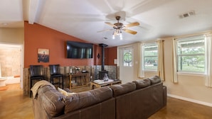 A living room with a brown leather sofa, a ceiling fan, a fireplace, and a TV mounted on the wall.