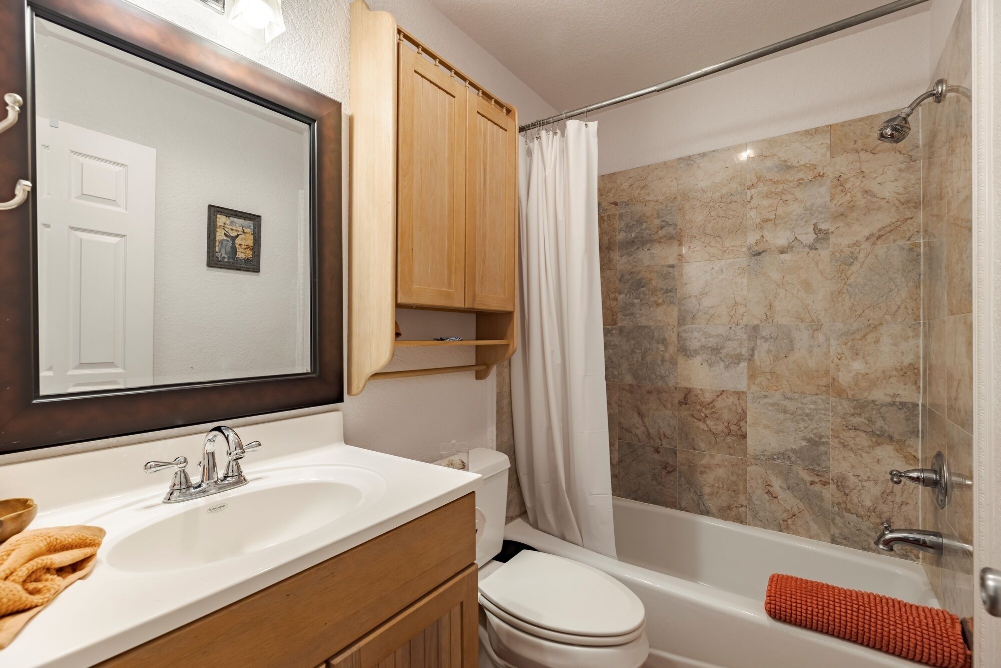 Een badkamer met een wastafel, spiegel, houten kastjes, toilet en douche met marmeren tegels.