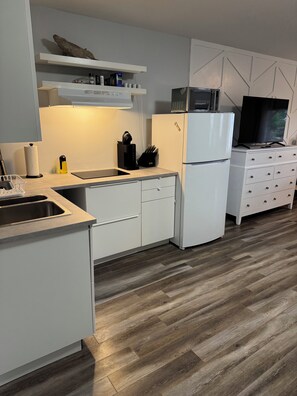 A modern kitchen with white cabinetry, a built-in microwave, a refrigerator, and a flat-screen TV.