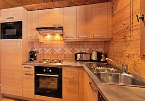 A modern kitchen with wooden cabinetry, a built-in oven, a stovetop, and a stainless steel sink. - Casa-Chalet Brizolée avec vue sur le lac à Tignes (Tignes)