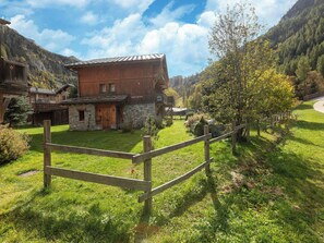 A rustic chalet with a stone foundation, wooden exterior, and a wooden fence in a mountainous area.