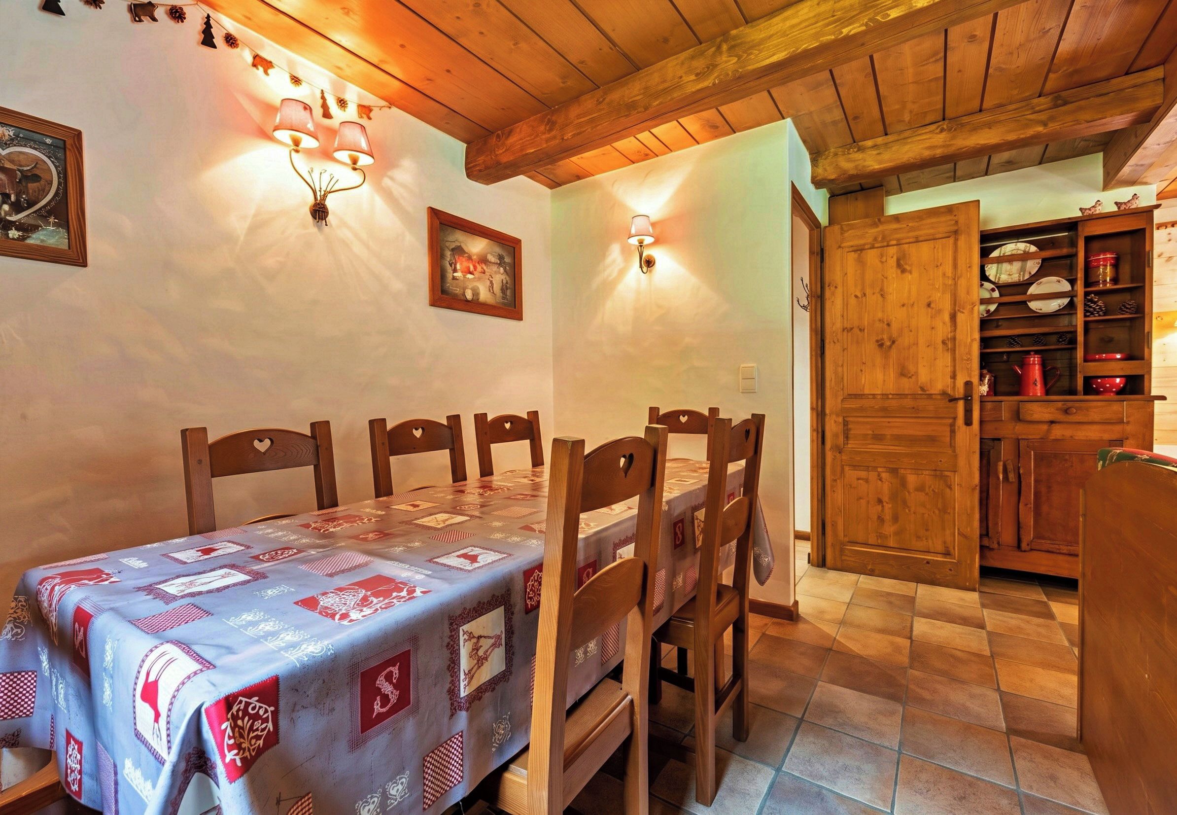 A dining area with a table set for four, wooden chairs, a wall-mounted light fixture, and a wooden cabinet with dishes.