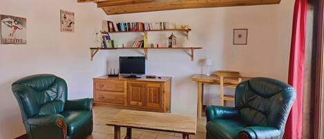 Una sala de estar con dos sillones de cuero verde, una mesa de madera, un televisor sobre un mueble de madera y estanterías arriba.
