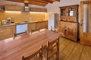 A kitchen with wooden cabinets, a dining table, chairs, a stove, and a refrigerator.