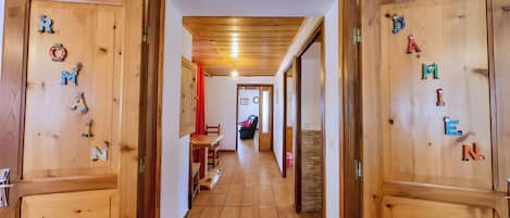 A wooden hallway with doors labeled with letters, a bench, and a chair in the background.