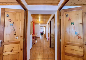 A wooden hallway with doors labeled with letters, a bench, and a chair in the background.