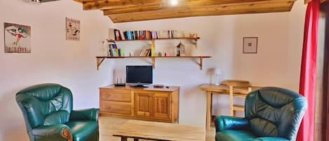 Sala de estar con dos sillones de cuero verde, una mesa de centro de madera, un televisor sobre un mueble de madera y estanterías arriba.
