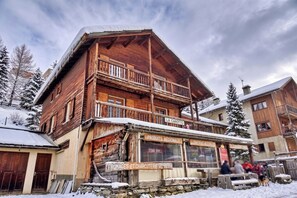 A wooden building with a balcony, signs for 'PRODUCTS RÉGIONAUX' and 'FROMAGES ET CHARCUTERIE DES MATEES', and a stone wall in front. - Casa-La Carotto Appartement pour 6 dans chalet (Molines-en-Queyras)