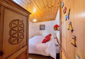 Une pièce en bois avec un lit, une armoire en bois ornée de motifs géométriques, une lampe fixée au mur et un tableau.