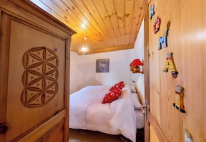 Ein Zimmer mit Holzboden, einem Bett, einem Holzschrank mit geometrischem Muster, einer Wandlampe und einem Gemälde.