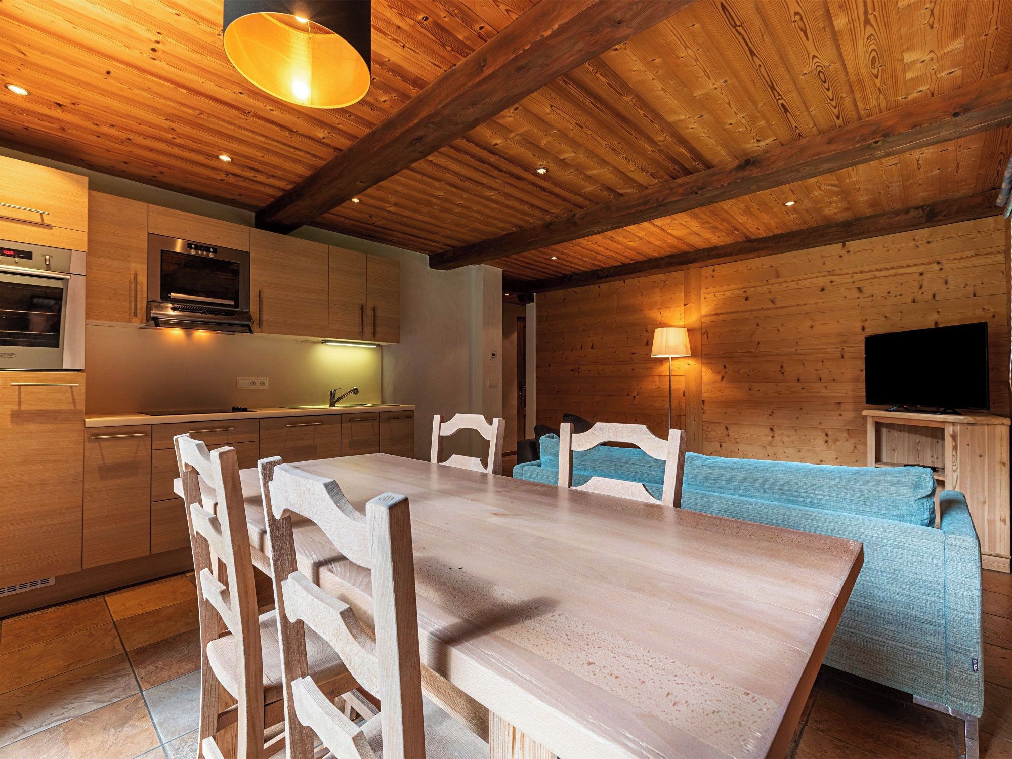 A wooden interior with a dining table, chairs, a sofa, a TV, and a kitchen area.