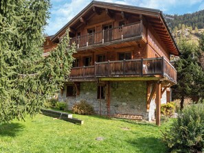 A wooden chalet with a stone foundation, a balcony, and a grassy yard.
