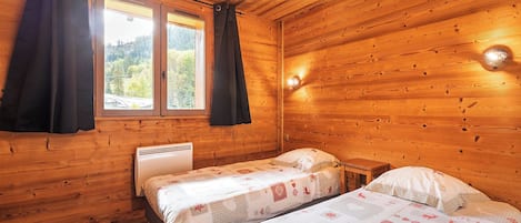 A wooden cabin room with two beds, a window, and a heater.
