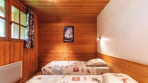 Habitación de cabaña de madera con dos camas, una ventana con cortinas, un cuadro enmarcado en la pared y una lámpara en el techo.