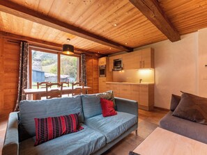 A cozy cabin interior with a wooden ceiling, a sofa, a dining table with chairs, and a kitchenette.