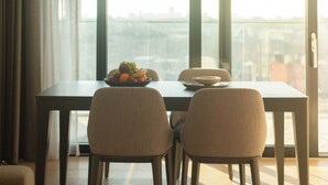 A dining area with a table and two chairs, a bowl of fruit, and a view of a cityscape through large windows. - Enclave KX - Campus Accommodation (London)