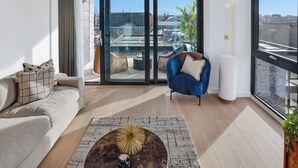 A modern living room with a sofa, a blue chair, a coffee table, and a view of the city through large windows. - Enclave KX - Campus Accommodation (London)