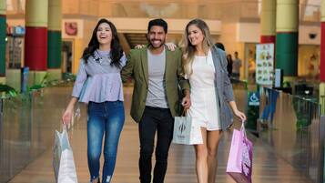 Três pessoas caminham por um corredor de um shopping carregando sacolas de compras.