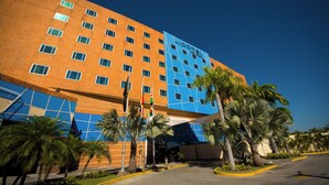 Un hotel moderno con fachada azul y naranja, varios pisos y palmeras en primer plano.