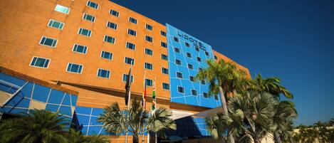 A modern hotel with a blue and orange facade, multiple floors, and palm trees in the foreground.