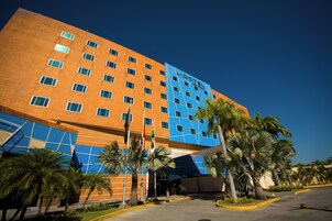 Un hotel moderno con fachada azul y naranja, varios pisos y palmeras en primer plano.