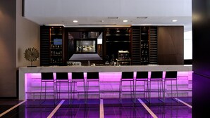 Un área de bar moderna con una barra larga, varios taburetes altos y una pantalla de televisión.