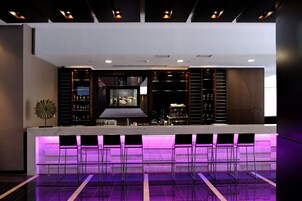 Uma área de bar moderna com um balcão comprido, vários banquinhos e uma tela de televisão.