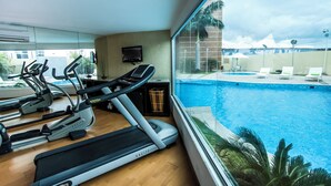 Un gimnasio con cintas de correr y máquinas elípticas, un televisor y vistas a una piscina.