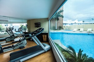 Uma academia com esteiras e elípticos, uma televisão e vista para uma piscina.