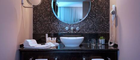 Une salle de bain avec un miroir rond, un lavabo blanc et un sèche-cheveux fixé au mur.