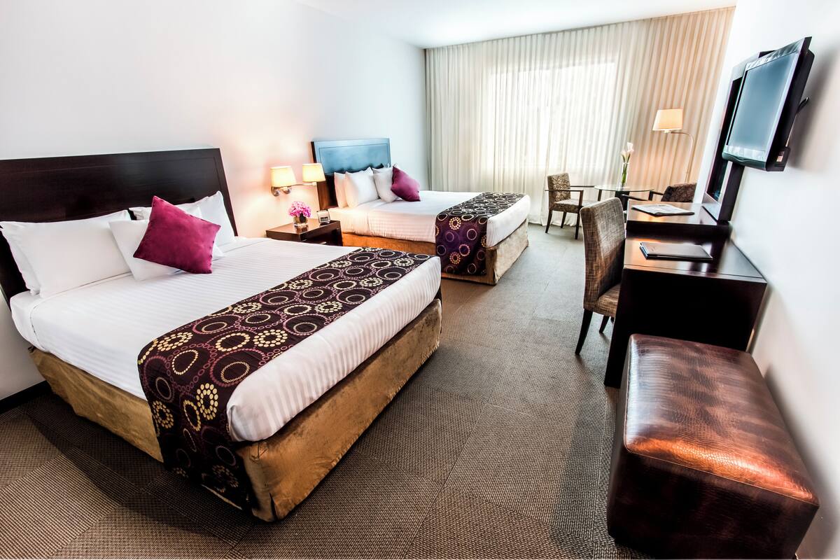 Habitación de hotel con dos camas, un escritorio, una silla, un televisor y una ventana con cortinas.