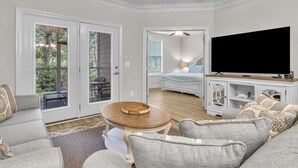 A spacious living room with a large TV, comfortable seating, and a view of the backyard through glass doors.