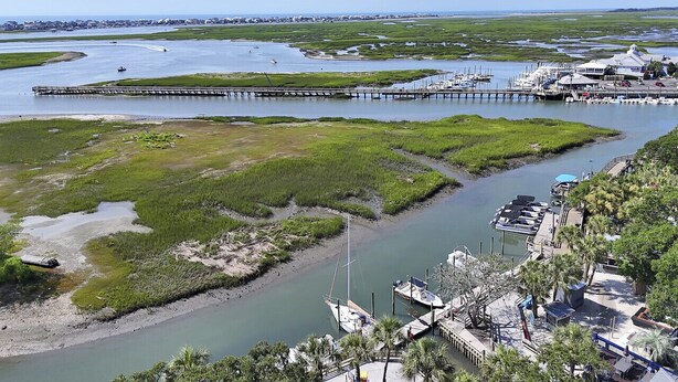A coastal area with a pier extending into the water, boats docked at the pier, and a marina with boats and a building.
