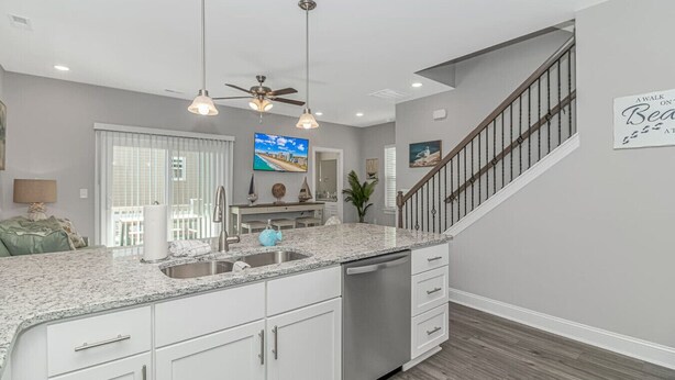 A modern kitchen with granite countertops, white cabinetry, a built-in dishwasher, and a ceiling fan.