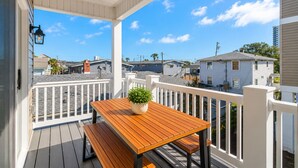 A covered porch with a wooden table and bench, a potted plant, and a white railing.