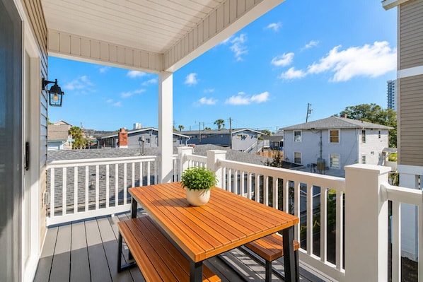 A covered porch with a wooden table and bench, a potted plant, and a white railing.