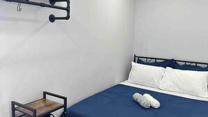 Un letto singolo con materasso blu e cuscini bianchi, un tavolino di legno e un gancio a parete.