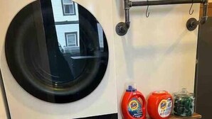 Una lavanderia compatta con due ante, dotata di lavatrice e asciugatrice integrate. Su uno scaffale sopra l'asciugatrice si trovano due flaconi di detersivo e un vasetto di ammorbidente.