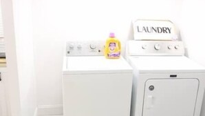 Una màquina de rentar blanca amb un gots de detergent groc i un cartell que diu "LAUNDRY" a la part superior.
