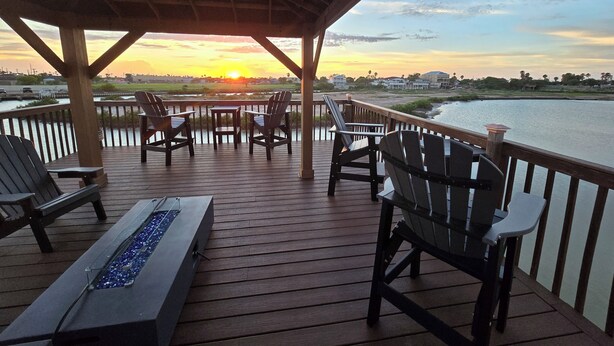 A wooden deck with chairs and a table, overlooking a body of water and a sunset. - Discover Your Dream Waterfront Getaway in Port Isabel, Texas! (Port Isabel)
