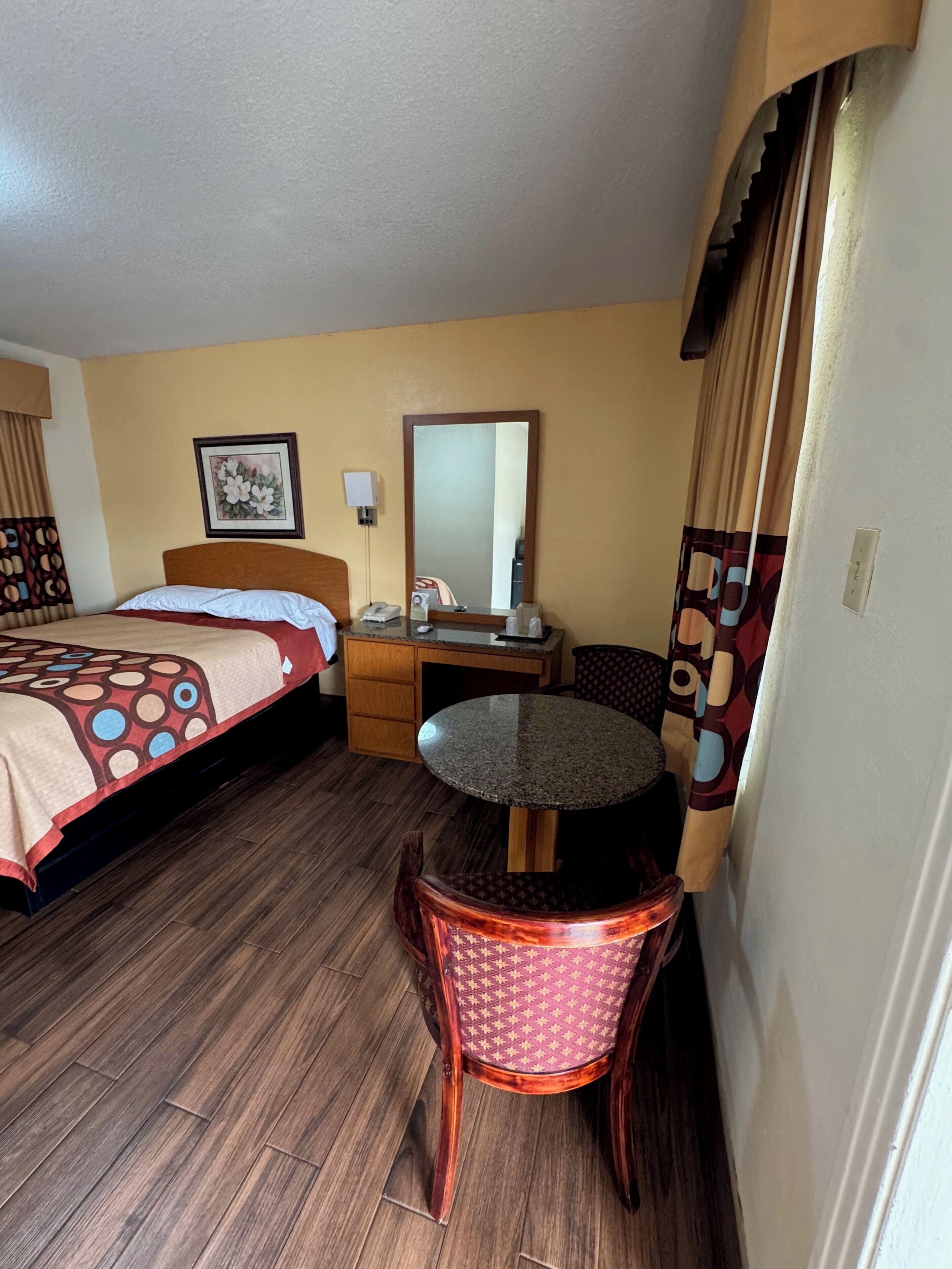 Une chambre d’hôtel comprenant un lit, un bureau avec une chaise, une table ronde, un miroir et un téléphone fixé au mur.